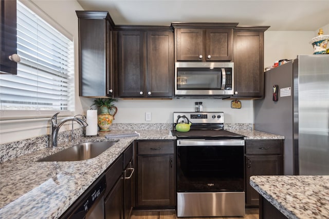 kitchen featuring dark brown cabinets, light stone counters, stainless steel appliances, and a sink