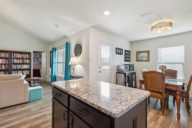 kitchen with light wood-style flooring, light stone countertops, visible vents, vaulted ceiling, and a center island