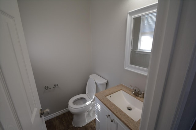 half bath featuring baseboards, vanity, toilet, and wood finished floors