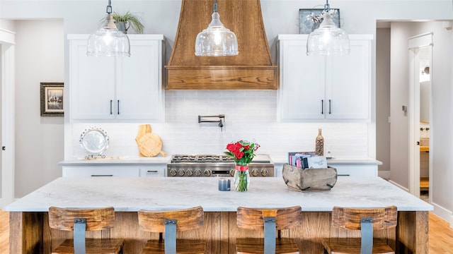 kitchen featuring a breakfast bar area, stove, white cabinets, custom exhaust hood, and backsplash