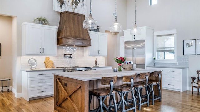 kitchen featuring light wood finished floors, custom range hood, a kitchen island, stainless steel appliances, and a kitchen bar