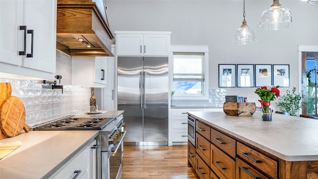 kitchen with custom exhaust hood, brown cabinetry, white cabinetry, and high end appliances