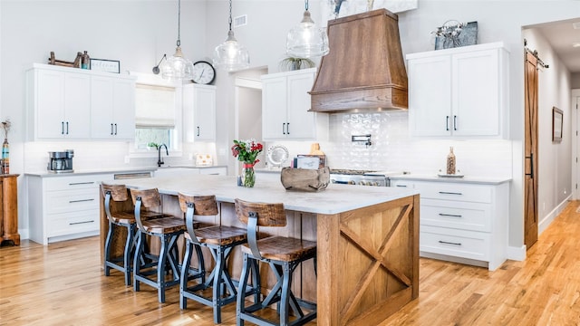 kitchen with light wood finished floors, visible vents, custom range hood, a kitchen island, and a kitchen breakfast bar