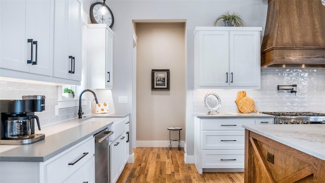 kitchen with baseboards, custom exhaust hood, light wood-type flooring, white cabinetry, and a sink