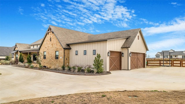 view of home's exterior featuring driveway, a garage, stone siding, fence, and board and batten siding