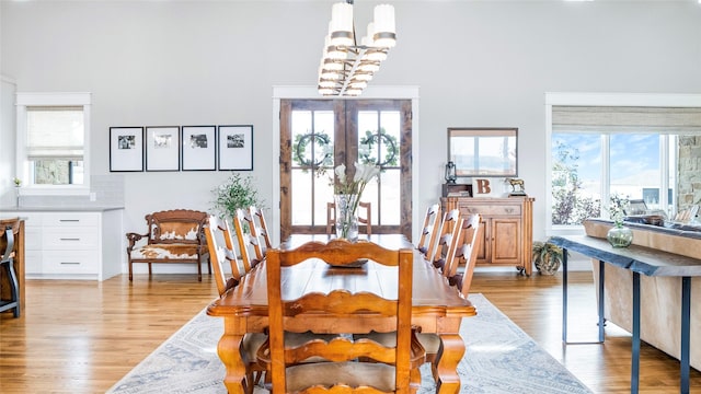 dining space with light wood-type flooring, french doors, and an inviting chandelier