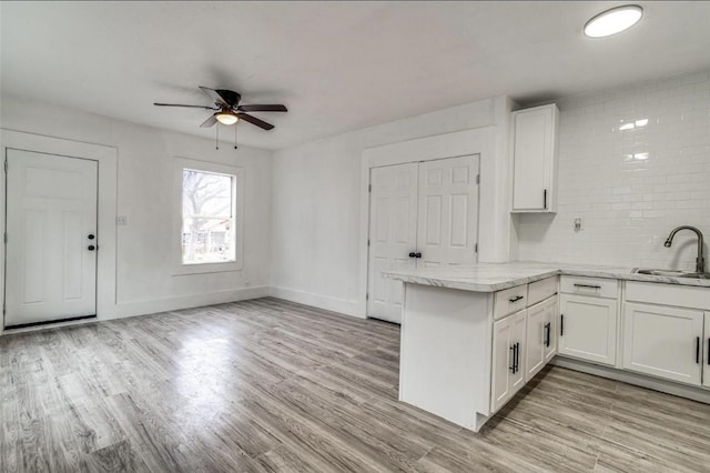 kitchen with decorative backsplash, white cabinets, a peninsula, light wood-style floors, and a sink