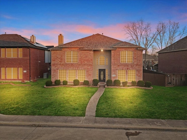 view of front facade featuring brick siding, a yard, central AC unit, and fence