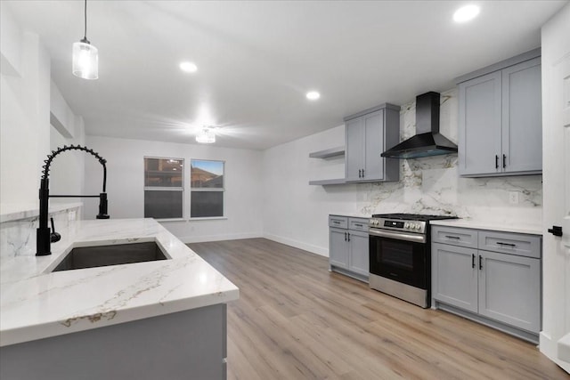 kitchen with gray cabinets, backsplash, gas stove, a sink, and wall chimney exhaust hood