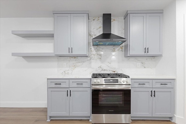 kitchen featuring gas stove, wall chimney range hood, gray cabinetry, and open shelves