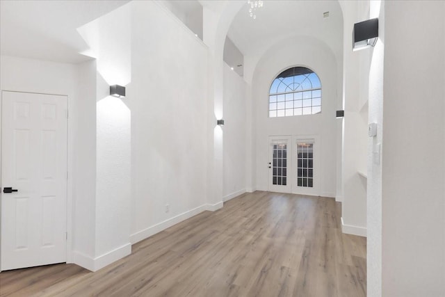 foyer with a towering ceiling, baseboards, wood finished floors, and french doors