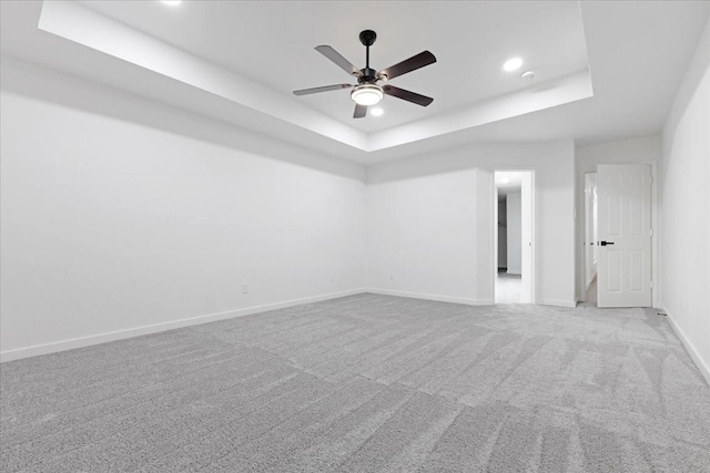 empty room with a ceiling fan, a tray ceiling, light colored carpet, and baseboards