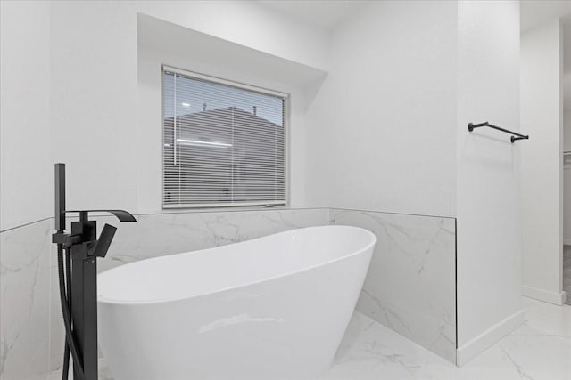 bathroom with a wainscoted wall, marble finish floor, a soaking tub, and tile walls