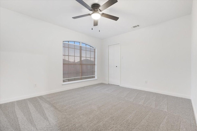 carpeted spare room with visible vents, ceiling fan, and baseboards