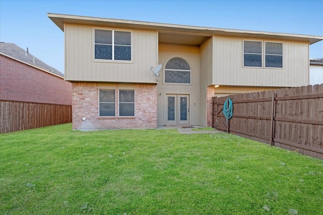 back of property with french doors, brick siding, a lawn, and a fenced backyard