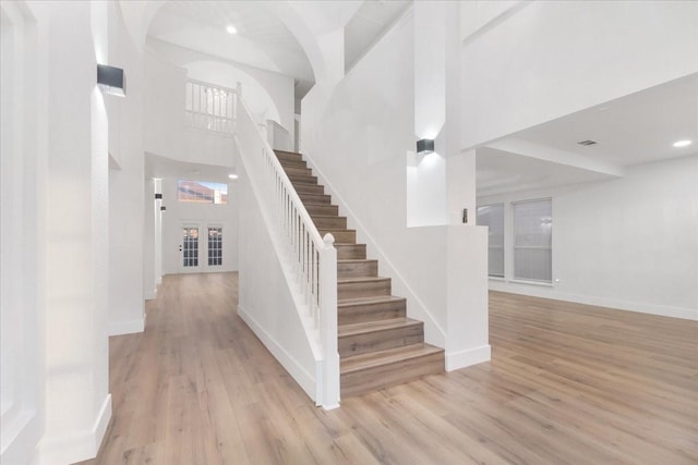 stairs with recessed lighting, wood finished floors, a towering ceiling, and baseboards