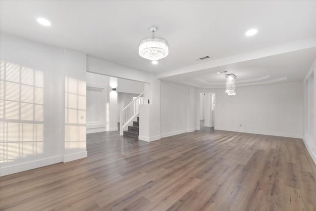 unfurnished room with a chandelier, wood finished floors, visible vents, and stairs