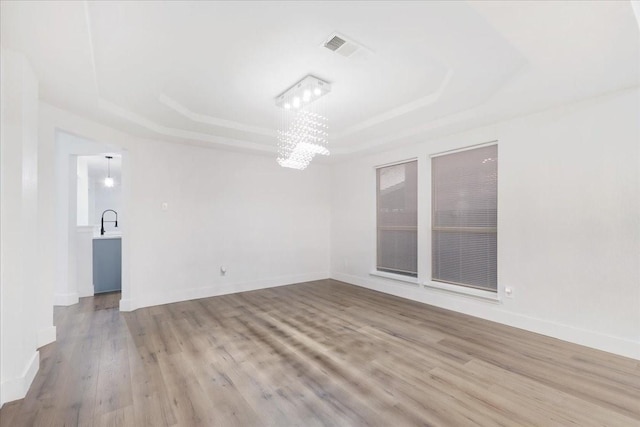 spare room featuring a raised ceiling, visible vents, baseboards, and wood finished floors