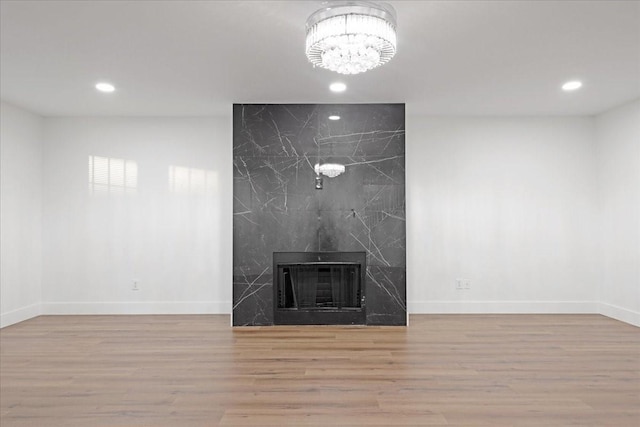 unfurnished living room featuring recessed lighting, an inviting chandelier, a premium fireplace, wood finished floors, and baseboards