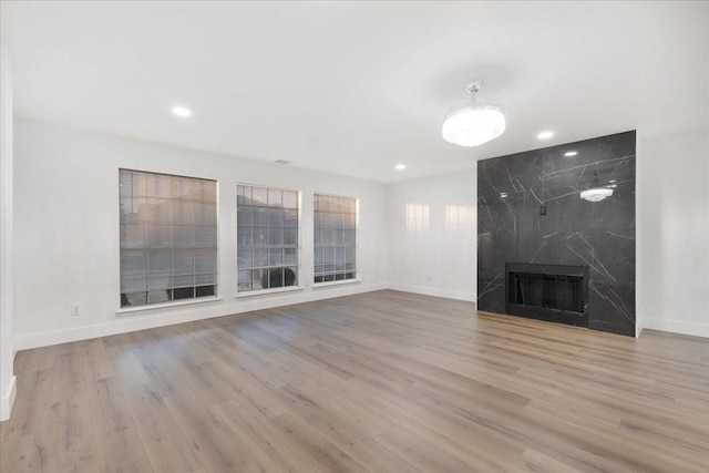 unfurnished living room with a high end fireplace, recessed lighting, baseboards, and wood finished floors