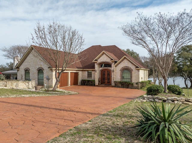 french provincial home with stone siding, french doors, decorative driveway, and an attached garage