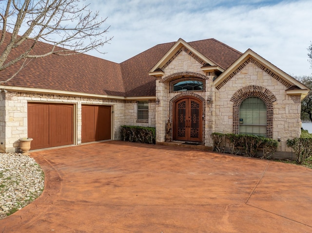 french provincial home with a garage, roof with shingles, concrete driveway, and french doors