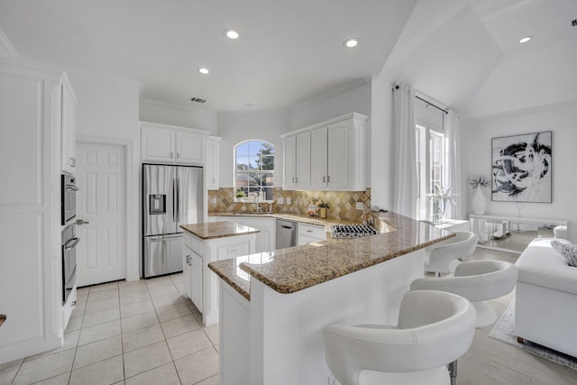 kitchen with tasteful backsplash, a kitchen island, appliances with stainless steel finishes, a peninsula, and light stone countertops