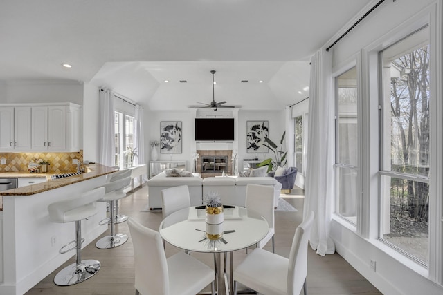 dining room with ceiling fan, recessed lighting, wood finished floors, vaulted ceiling, and a tiled fireplace