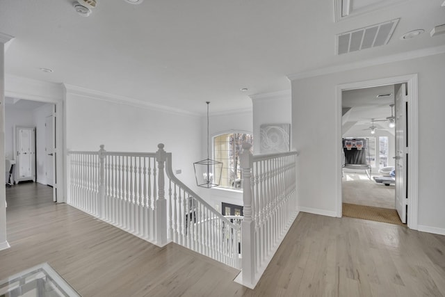 hallway with crown molding, a notable chandelier, visible vents, wood finished floors, and baseboards