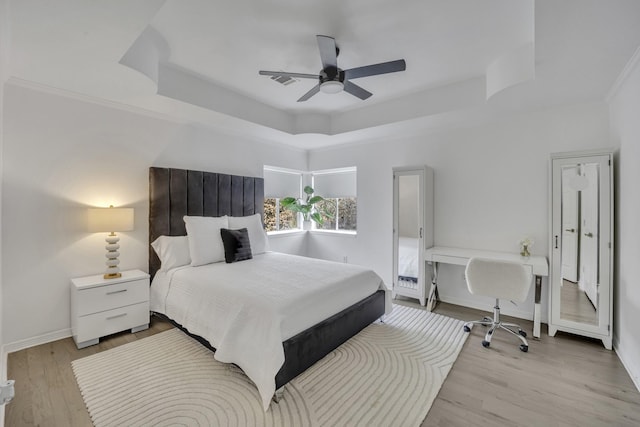 bedroom with a ceiling fan, visible vents, baseboards, light wood finished floors, and a raised ceiling