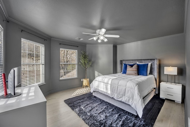 bedroom featuring a ceiling fan, visible vents, crown molding, and wood finished floors