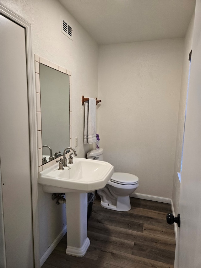 half bath featuring visible vents, wood finished floors, toilet, and baseboards