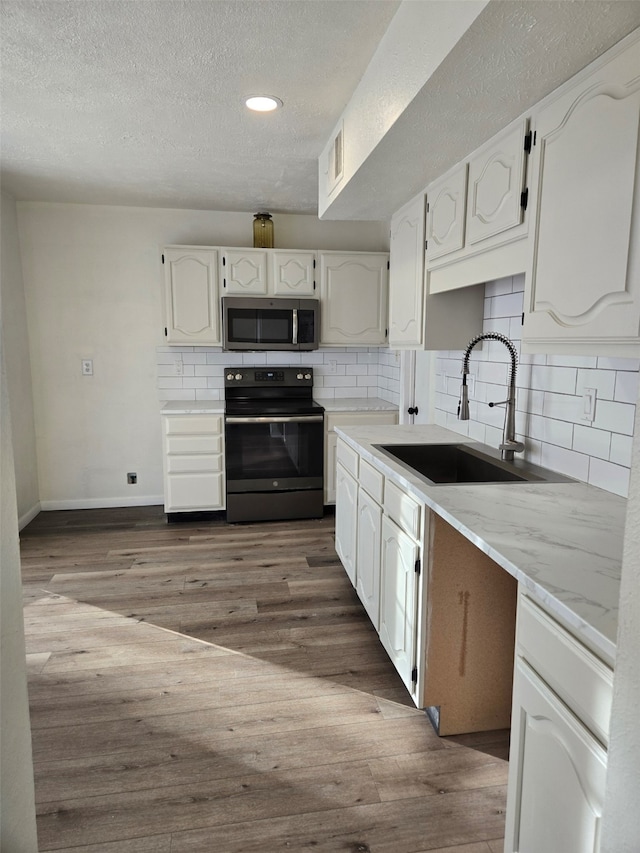 kitchen featuring decorative backsplash, stainless steel microwave, black electric range oven, wood finished floors, and a sink