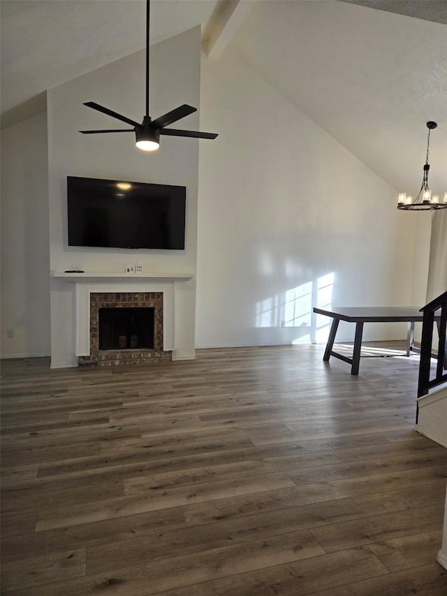 unfurnished living room with a fireplace with raised hearth, ceiling fan with notable chandelier, dark wood-style floors, and beam ceiling