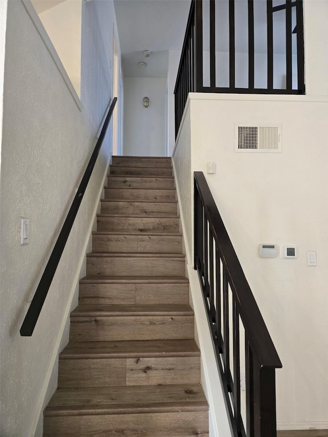 staircase with visible vents, wood finished floors, and a textured wall