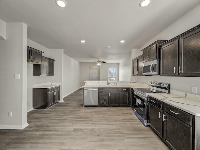 kitchen featuring light wood-style flooring, ceiling fan, appliances with stainless steel finishes, a peninsula, and a sink