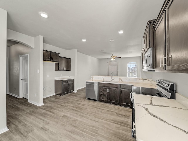 kitchen featuring light stone countertops, stainless steel appliances, dark brown cabinets, light wood-type flooring, and a sink