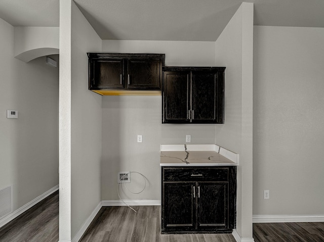 clothes washing area with arched walkways, wood finished floors, visible vents, and baseboards