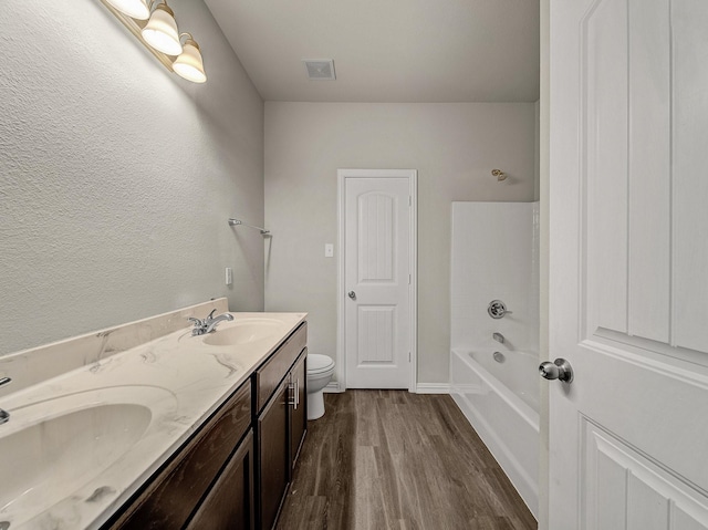 bathroom with toilet, double vanity, a sink, and wood finished floors