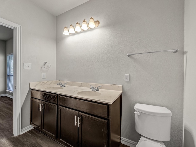 bathroom with double vanity, toilet, a sink, wood finished floors, and baseboards