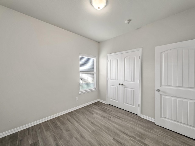 unfurnished bedroom with a closet, wood finished floors, and baseboards