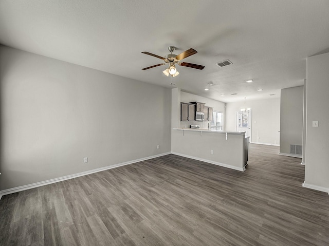 unfurnished living room featuring ceiling fan with notable chandelier, dark wood finished floors, and visible vents