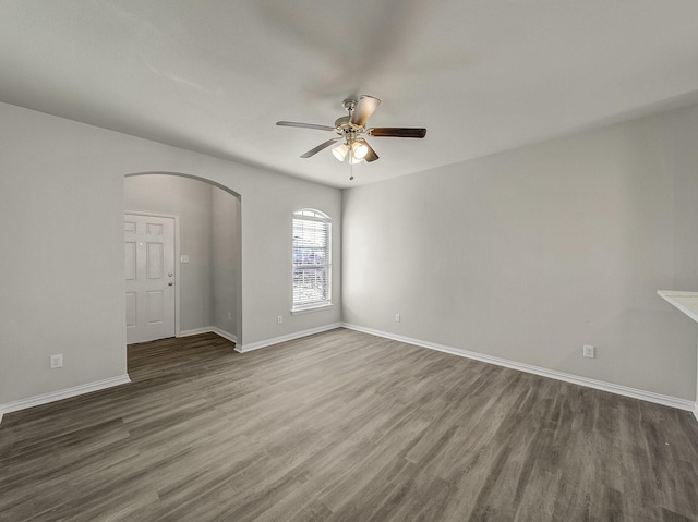 spare room with arched walkways, ceiling fan, baseboards, and wood finished floors