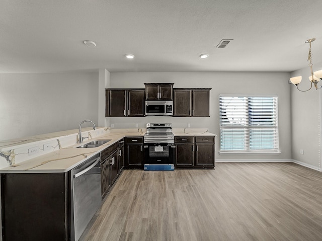 kitchen with an inviting chandelier, light wood-style flooring, appliances with stainless steel finishes, and a sink