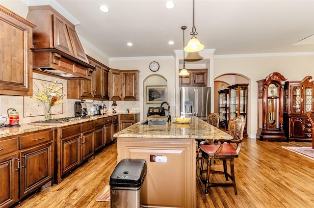 kitchen featuring a center island with sink, arched walkways, stainless steel appliances, premium range hood, and a sink