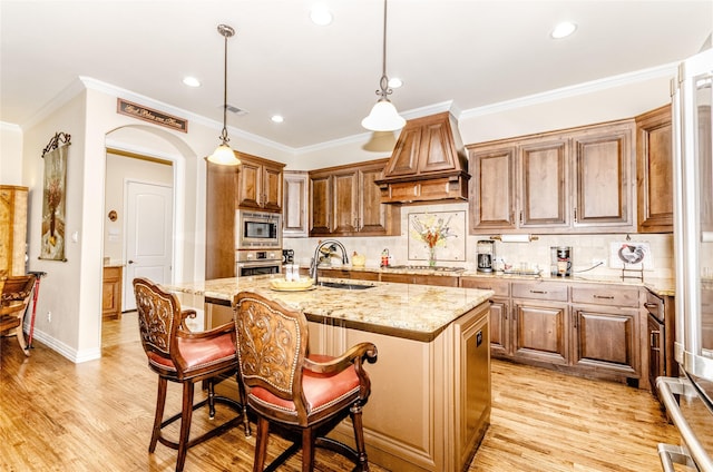 kitchen with arched walkways, light stone counters, appliances with stainless steel finishes, premium range hood, and a sink