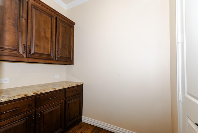 kitchen with baseboards, dark wood-style floors, ornamental molding, light stone countertops, and dark brown cabinets