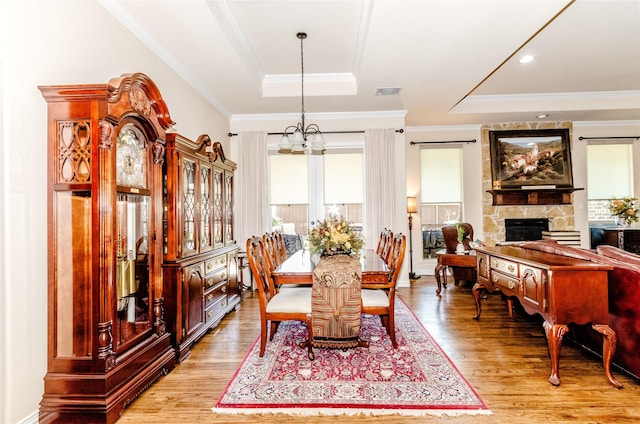 dining area with light wood-style floors, a raised ceiling, crown molding, and a stone fireplace