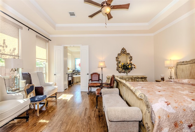 bedroom with crown molding, visible vents, a raised ceiling, and wood finished floors