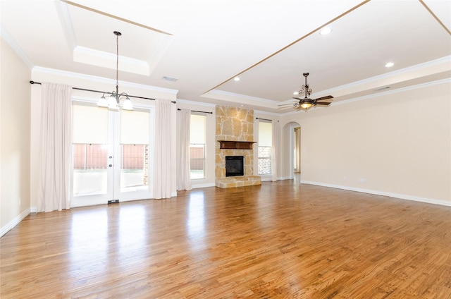 unfurnished living room featuring ceiling fan with notable chandelier, a fireplace, baseboards, light wood finished floors, and a raised ceiling